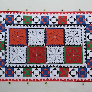 May include: A white fabric wall hanging with a geometric pattern in red, blue, green, and black. The pattern is made up of squares and triangles.