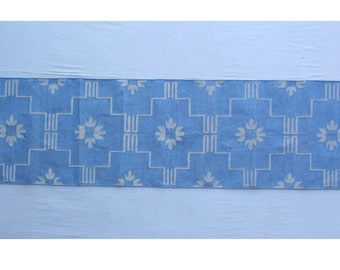 May include: A blue and white patterned runner rug with a geometric design. The rug has a light blue background with white geometric shapes and a white border.