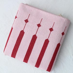 Puede incluir: Textil plegado de color rosa y rojo con estampado. El textil presenta rayas rojas verticales que se alternan con rayas rosas. Formas de diamante rojas est&aacute;n conectadas por l&iacute;neas finas. El textil est&aacute; plegado y parece estar hecho de tela tejida.
