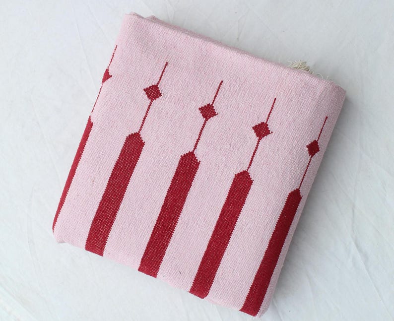 Puede incluir: Textil plegado de color rosa y rojo con estampado. El textil presenta rayas rojas verticales que se alternan con rayas rosas. Formas de diamante rojas est&aacute;n conectadas por l&iacute;neas finas. El textil est&aacute; plegado y parece estar hecho de tela tejida.