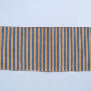 May include: A long, narrow rug with alternating stripes of light brown and dark blue. The rug has a fringed edge.
