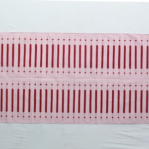 Puede incluir: Textil rectangular rosa con un patr&oacute;n repetitivo de l&iacute;neas verticales burdeos y formas de diamante. El dise&ntilde;o es sim&eacute;trico, con dos filas del patr&oacute;n. El textil es probablemente un art&iacute;culo decorativo.