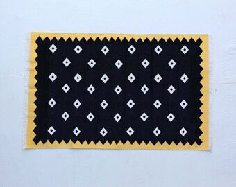 May include: A black and white geometric rug with a yellow border. The rug has a repeating pattern of white diamonds on a black background.
