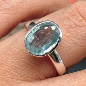 Op de afbeelding: Een zilveren ring met een lichtblauwe ovale edelsteen.