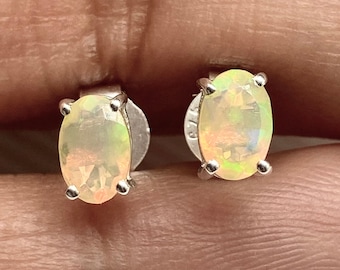 May include: A pair of silver opal earrings with oval-shaped stones. The opals have a light yellow and white color with a hint of green.