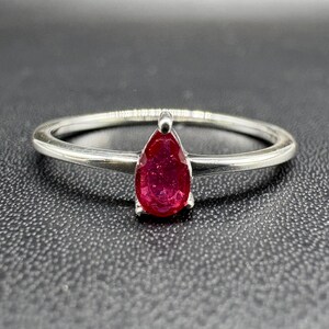 May include: A silver ring with a pear-shaped ruby gemstone.