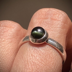 May include: A silver ring with a black and green gemstone set in a bezel setting.