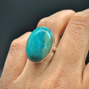 May include: A silver ring with a large oval turquoise gemstone. The gemstone has a blue and green color with brown inclusions.