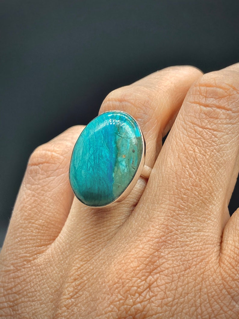 May include: A silver ring with a large oval turquoise gemstone. The gemstone has a blue and green color with brown inclusions.