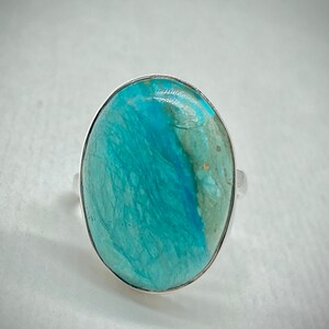 May include: A silver ring with a large oval turquoise gemstone. The turquoise is a vibrant blue-green color with white and gold veins.