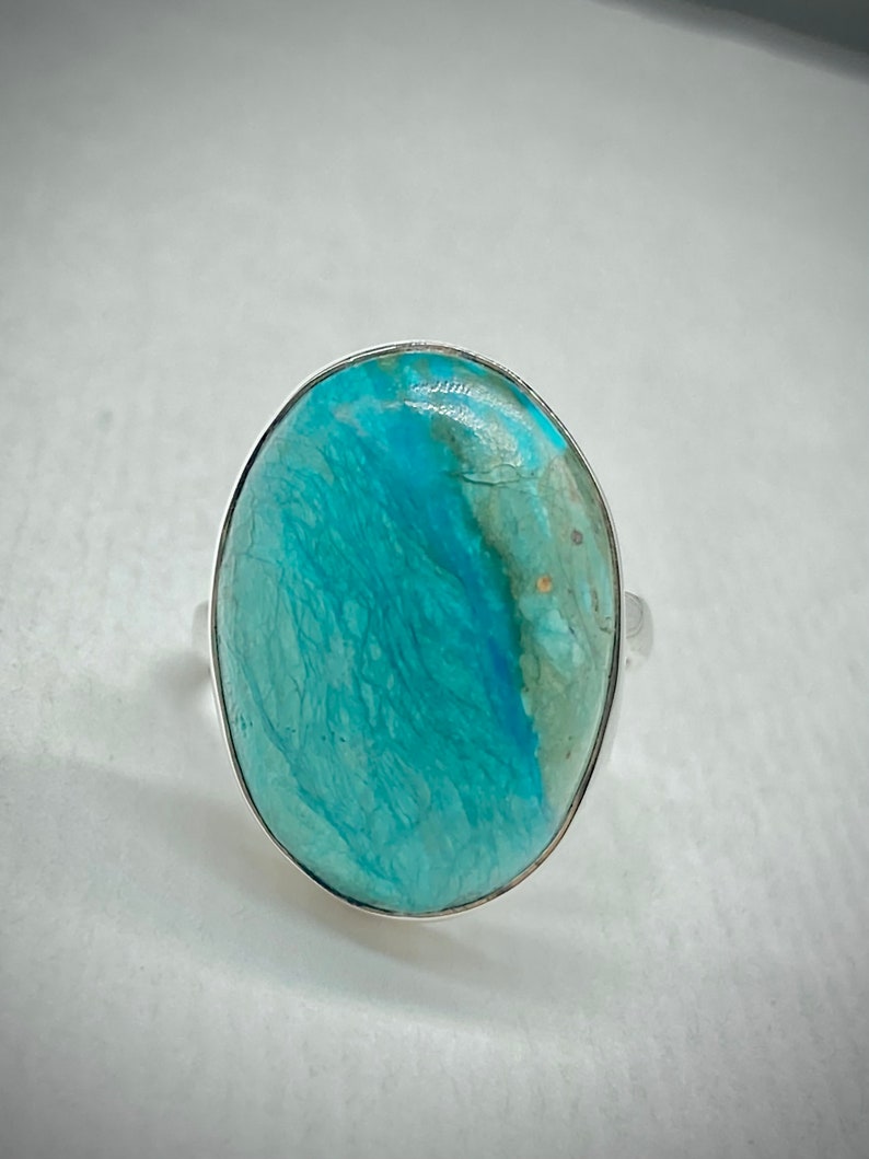 May include: A silver ring with a large oval turquoise gemstone. The turquoise is a vibrant blue-green color with white and gold veins.