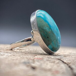 May include: A silver ring with a large oval turquoise gemstone. The turquoise is a mottled blue-green color.