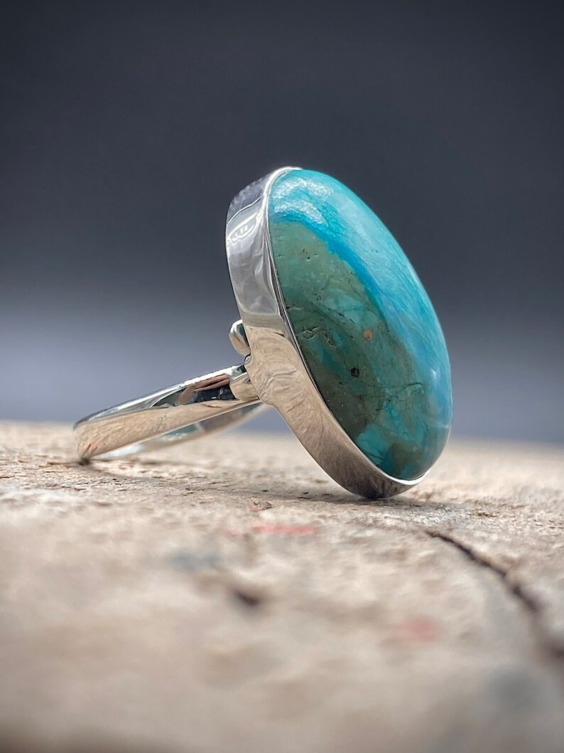 May include: A silver ring with a large oval turquoise gemstone. The turquoise is a mottled blue-green color.