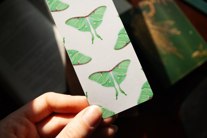 Pode incluir: Um marcador branco com um padr&atilde;o repetido de mariposas luna verdes. As mariposas t&ecirc;m um corpo verde claro e asas com uma borda verde mais escura. As asas t&ecirc;m uma mancha branca de cada lado.