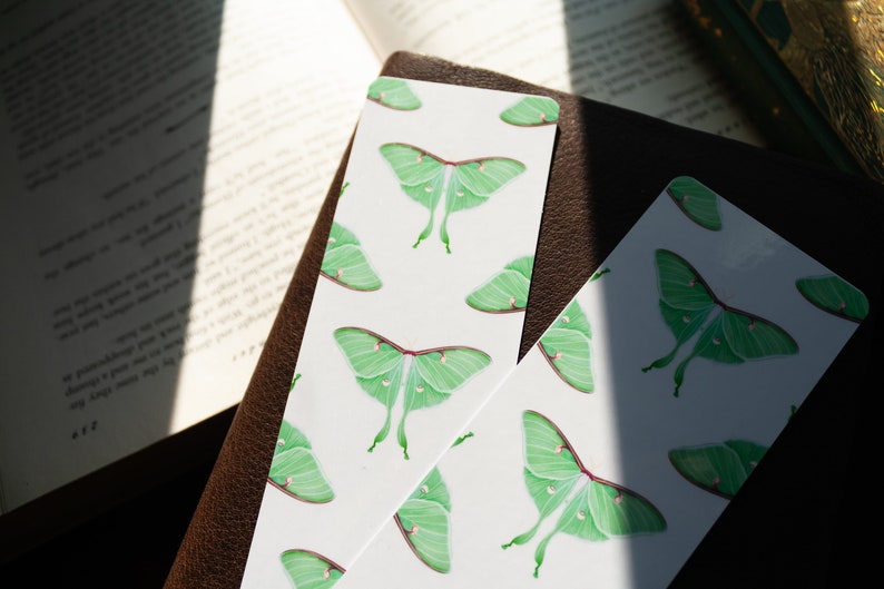 Pode incluir: Dois marcadores de p&aacute;gina brancos com um padr&atilde;o repetido de mariposas luna verdes. As mariposas s&atilde;o ilustradas com asas detalhadas e um corpo verde claro.