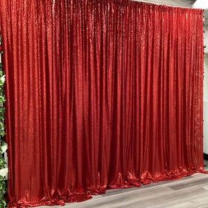 May include: A vibrant red sequin curtain hangs, creating a shimmering backdrop. The fabric drapes in vertical folds, catching the light and adding a touch of glamour. Ideal for events and photo shoots.