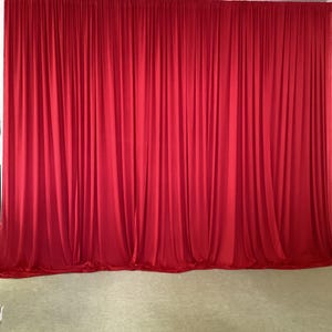 May include: A red stage curtain backdrop with pleats, hanging from a white ceiling.