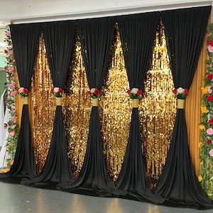 May include: A decorative event backdrop featuring a shimmering gold sequin curtain layered behind five black fabric drapes. Each black drape is gathered and secured with a gold band adorned with a cluster of red, white, and pink artificial roses.