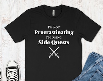 May include: Black t-shirt with white text that reads "I'm not procrastinating I'm doing side quests" with two crossed swords underneath the text.