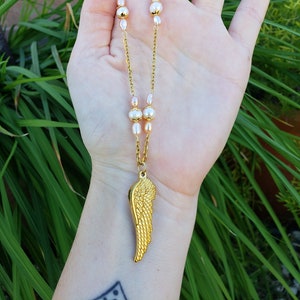 May include: A gold necklace with a single gold angel wing pendant and small white pearl beads.