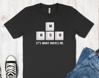 May include: Black t-shirt with a white graphic of the letters W, A, S, and D, which are the keys on a computer keyboard. The text below the keys reads "It's what moves me."