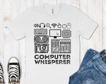 Op de afbeelding: Wit T-shirt met een zwart ontwerp van computerpictogrammen en de tekst "COMPUTER WHISPERER".