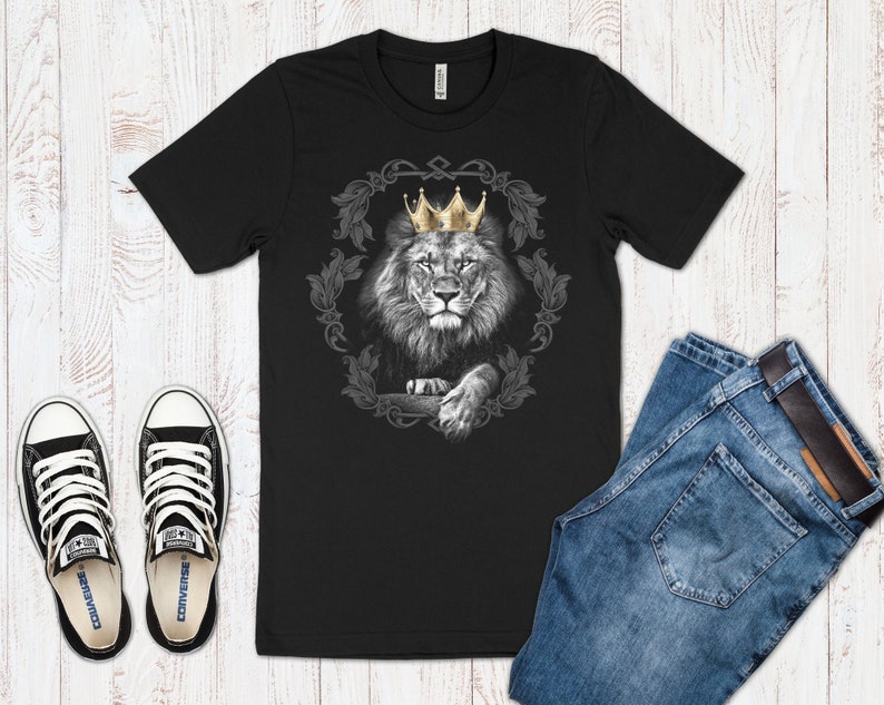 K&ouml;nnte beinhalten: Schwarzes T-Shirt mit einem Motiv eines L&ouml;wen, der eine goldene Krone tr&auml;gt. Der L&ouml;we ist von verzierten Blumenmustern umgeben.