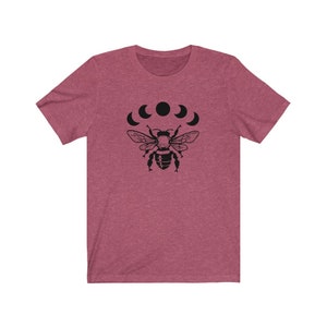 May include: A heather pink t-shirt with a black graphic of a bee with five crescent moons above it.