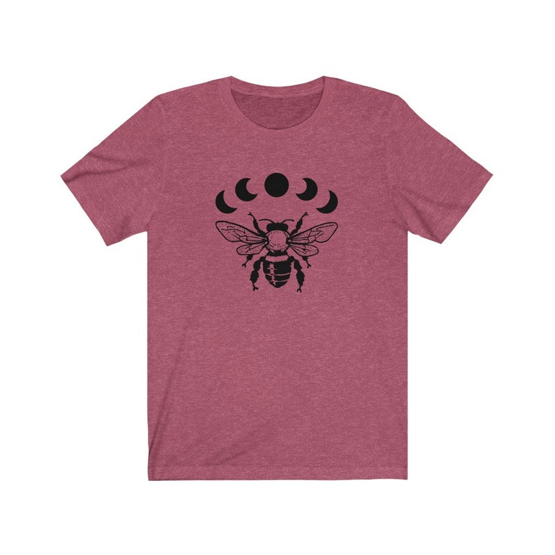 May include: A heather pink t-shirt with a black graphic of a bee with five crescent moons above it.