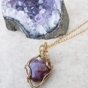 May include: A gold wire wrapped pendant featuring a heart-shaped red and white agate stone. The pendant is hanging from a gold chain.