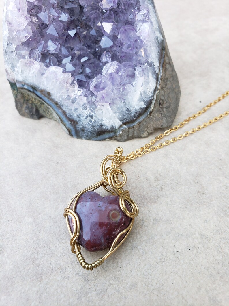 May include: A gold wire wrapped pendant featuring a heart-shaped red and white agate stone. The pendant is hanging from a gold chain.