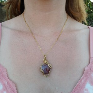 May include: A gold chain necklace with a pendant featuring a heart-shaped gemstone wrapped in gold wire.