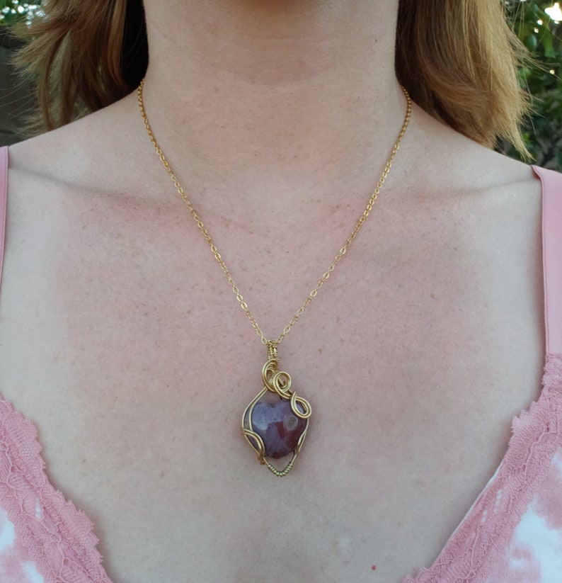 May include: A gold chain necklace with a pendant featuring a heart-shaped gemstone wrapped in gold wire.