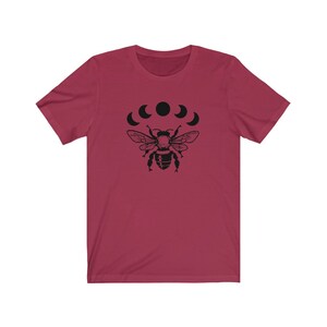 May include: A maroon t-shirt with a black bee and five black crescent moons printed on the front.