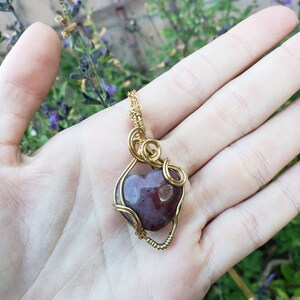 May include: A heart-shaped pendant made of red agate wrapped in gold wire. The pendant is hanging from a gold chain.