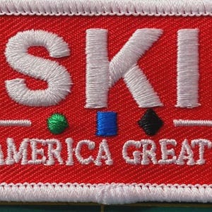 May include: A red embroidered patch with white text and a white border. The word "SKI" is at the top, with "MAKE AMERICA GREAT AGAIN" below. Small green, blue, and black shapes are under the "SKI".