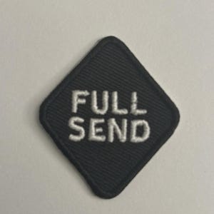 Puede incluir: Parche negro en forma de diamante con las palabras "FULL SEND" bordadas en blanco. El parche tiene una superficie texturizada y un borde cosido. Ideal para chaquetas, bolsos u otras prendas.