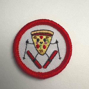 May include: Embroidered patch featuring a smiling pizza slice on skis, with ski poles. The pizza has toppings and a happy face. The patch is round, with a white center and a red border.