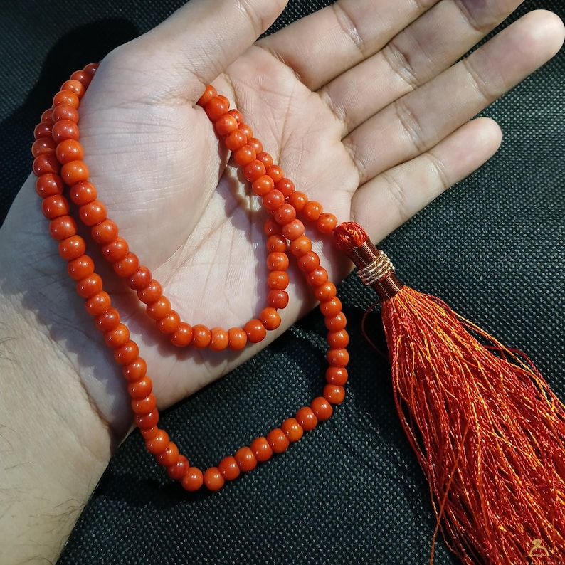 May include: Orange beaded necklace with a tassel. The necklace is made of small, round beads and has a long, orange tassel at the end. The beads are a vibrant orange color.
