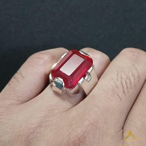 Puede incluir: Un anillo de plata con una gran gema roja brillante de forma rectangular. La gema tiene un centro rectangular m&aacute;s claro, casi blanco. El anillo est&aacute; engastado en una banda de plata con un dise&ntilde;o simple y cl&aacute;sico.