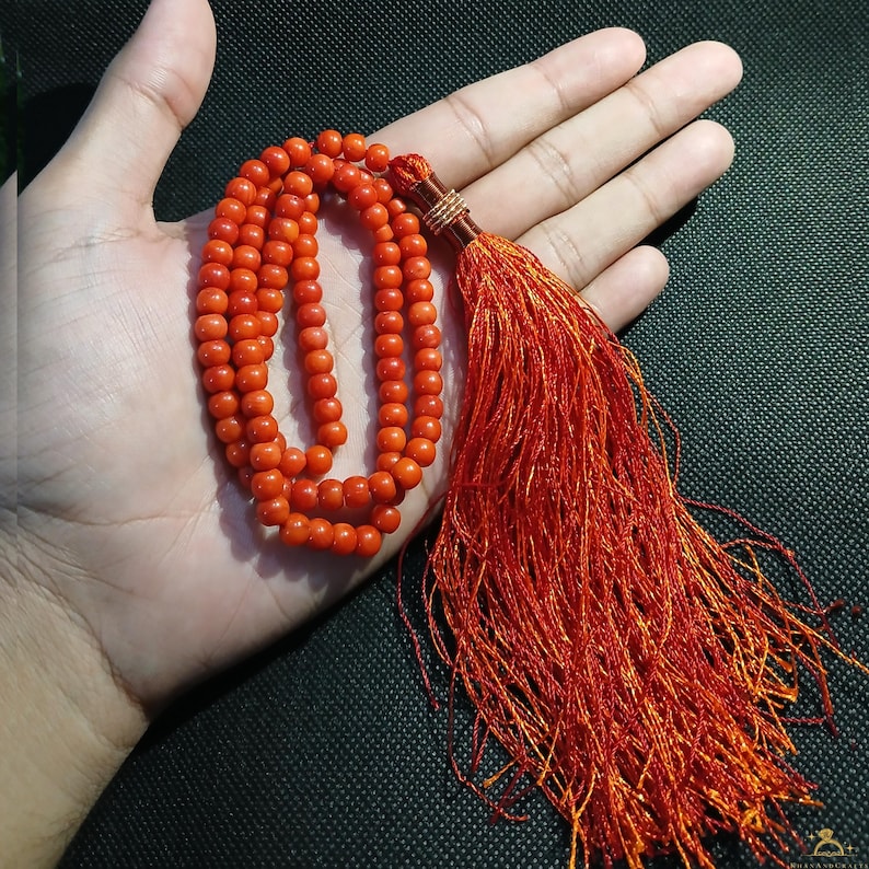 May include: A vibrant orange beaded necklace with a long, matching tassel. The necklace is composed of small, round beads. The tassel is made of numerous strands of orange thread, creating a flowing effect. The necklace is displayed on a hand.