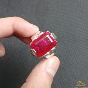 Puede incluir: Un anillo de plata con una gran gema roja rectangular. El anillo tiene un dise&ntilde;o simple y moderno con un acabado pulido. La gema es el punto focal, captando la luz y mostrando su color intenso.