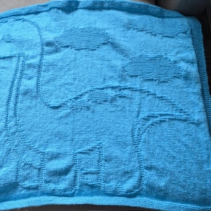 Puede incluir: Una manta de bebé de punto azul con un diseño de dinosaurio de punto blanco.