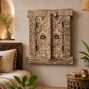 May include: A rectangular wooden wall panel featuring two hinged doors with intricate floral carvings and dark metal ring pulls. The light brown wood has a distressed finish, and the doors are secured with a small metal latch at the top center.