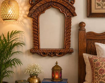 May include: A brown wooden wall-mounted mirror frame featuring an arched top and intricate carved leaf patterns along the sides. The frame includes a small horizontal shelf at the base and a decorative floral carving at the very top center.