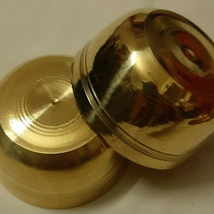May include: Two small, golden-colored brass bowls. The bowls have a rounded shape with a flat base and a slightly flared rim. The surface of the bowls is smooth and polished, reflecting light. The bowls appear to be handmade.