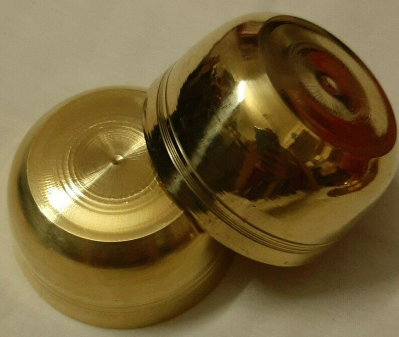 May include: Two small, golden-colored brass bowls. The bowls have a rounded shape with a flat base and a slightly flared rim. The surface of the bowls is smooth and polished, reflecting light. The bowls appear to be handmade.