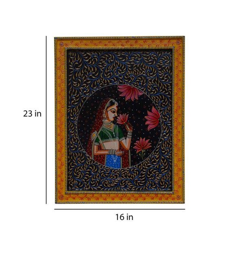 May include: A framed painting depicting a woman in traditional Indian attire, holding a flower. The painting is set against a dark blue background with intricate floral patterns. The frame is yellow with red and gold accents. The painting measures 40.6 cm by 58.4 cm.