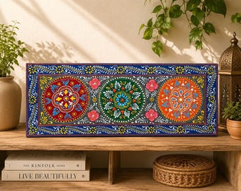 Puede incluir: Una pieza de arte mural rectangular que presenta tres diseños de mandalas circulares en rojo, verde y naranja sobre un fondo gris oscuro. El borde es azul profundo con patrones florales amarillos y blancos. La obra tiene detalles pintados.