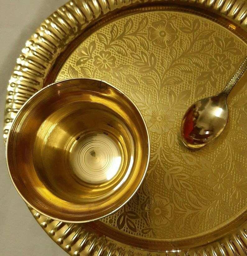 May include: A gold-colored metal serving set, including a small bowl, a spoon, and a round tray. The tray has a floral pattern and a ridged edge. The bowl and spoon are smooth and reflective, creating a warm, inviting aesthetic.